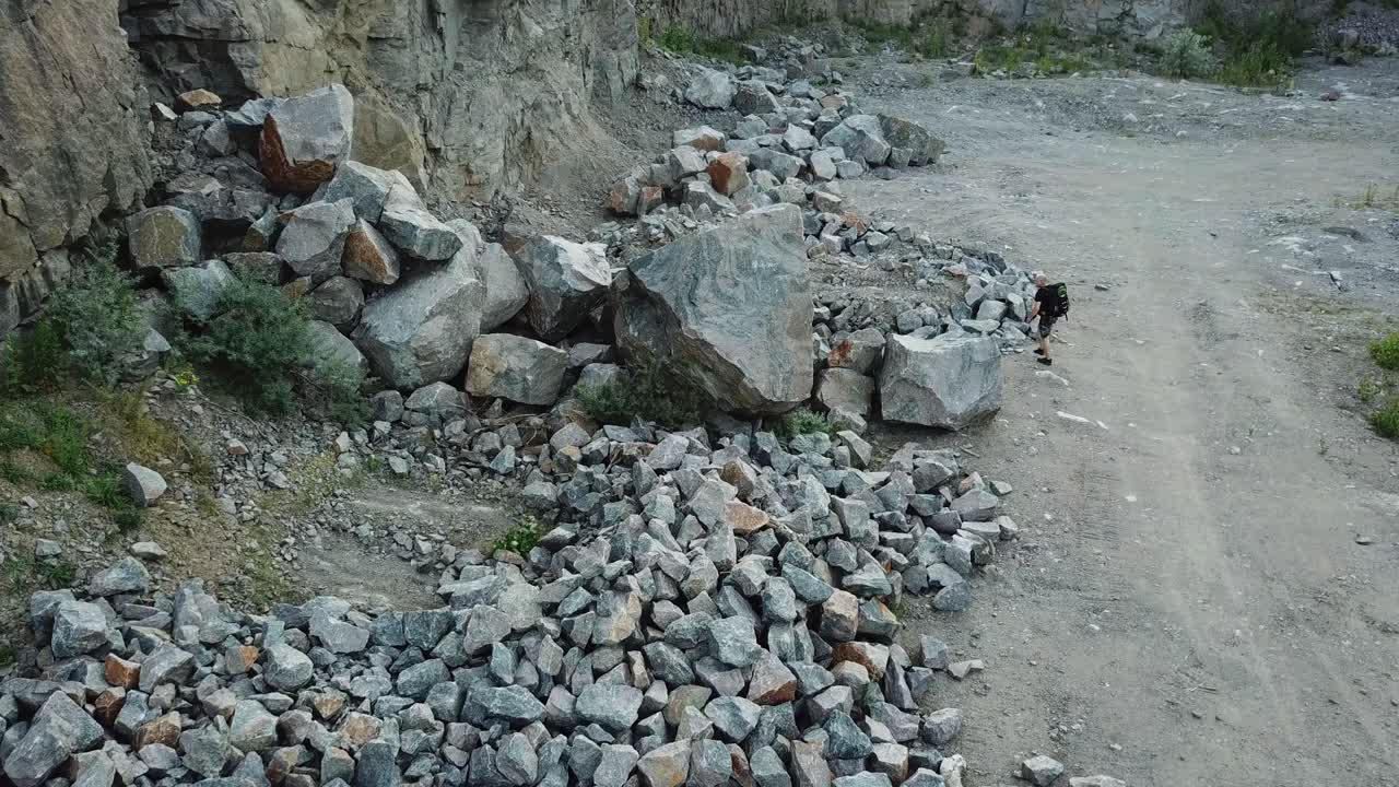 Hiker man going through the stone trail and comes into a rocky place. Aerial view of a tourist trekking in the mountains outdoors.