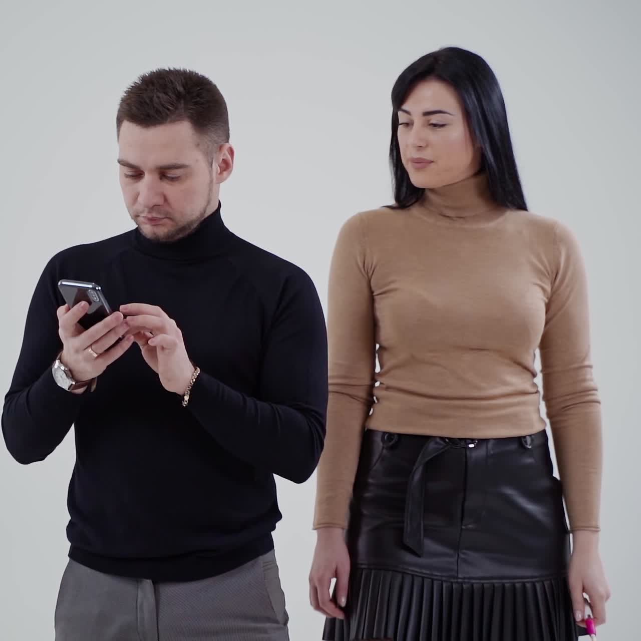 Portrait of a couple in the light studio. Handsome man looking into his cell phone. Beautiful woman coming to a man. Slow motion.