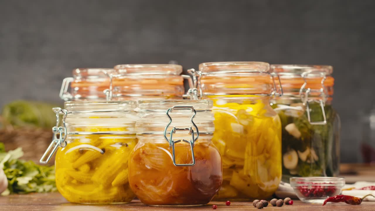 Fermented food in glass cans on table close-up. Preservation of vegetables in glass jars. Fermentation preserved mini corns, kimchi, cucumbers, mushrooms with spices.