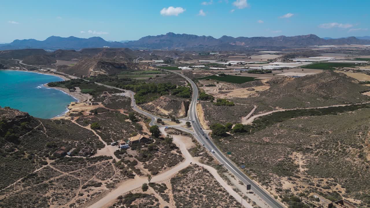 Aerial view of winding coastal roads, hills and farmland near Águilas in the Murcia region of Spain, showing blue shoreline, rugged terrain and summer landscapes under clear skies