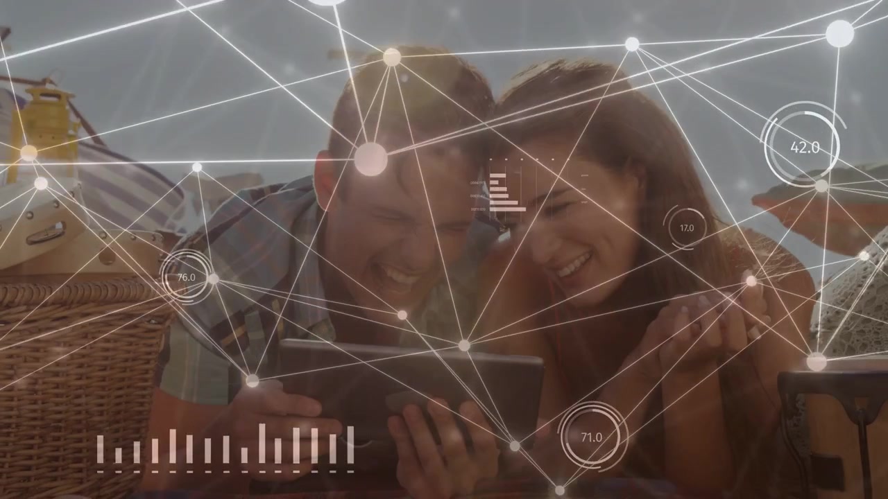 Couple tilting toward tablet on beach-picnic, watching content and showing animated tech HUD graphs