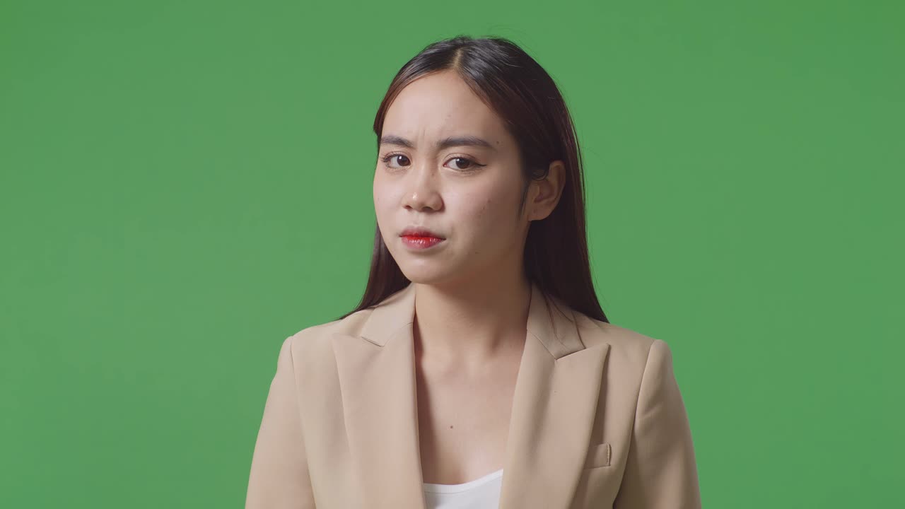녹색 스크린 앞에 서 있는 아시아 사업가 여성이 만족하지 않고 머리를 흔들고 있습니다.