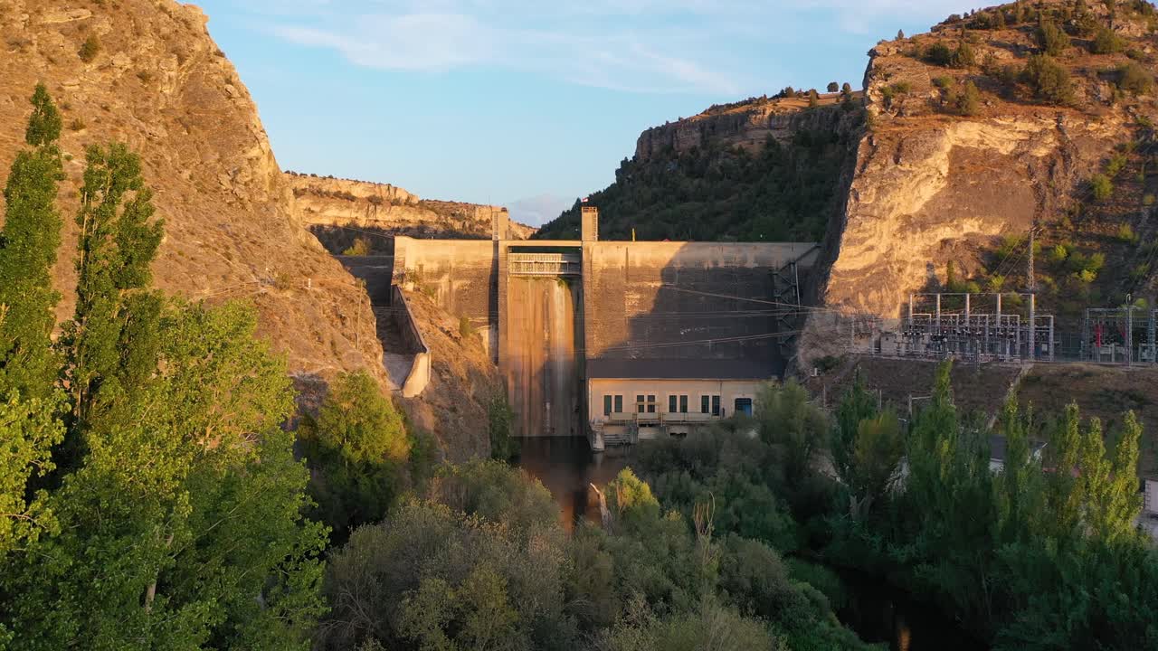 vuelo con un dron en un cañón hacia una presa donde se genera electricidad con árboles verdes a la orilla del río visualizando el curso de un río en una puesta de sol durante la hora dorada en verano segovia españa