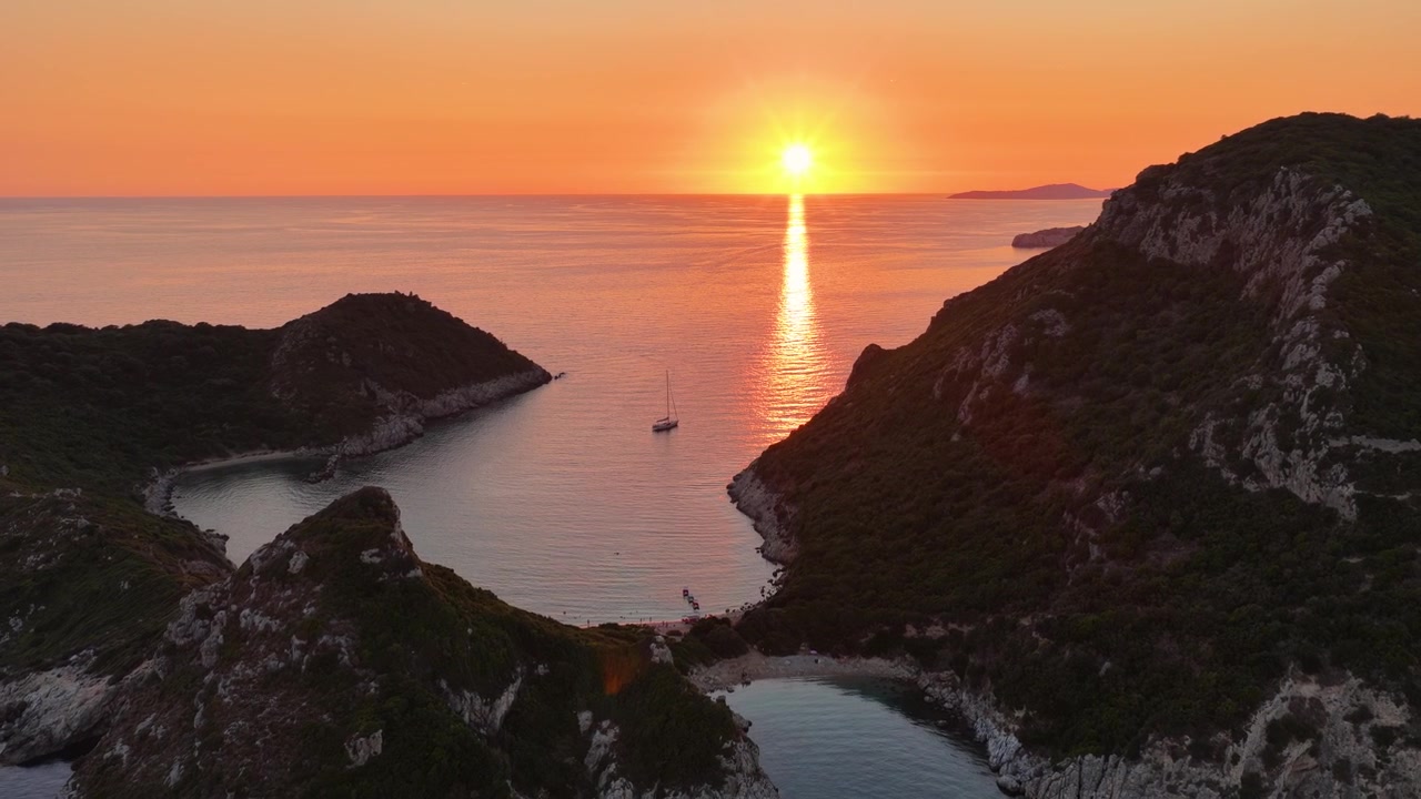 Veduta aerea panoramica della spiaggia gemella di Porto Timoni al tramonto a Corfù Nord, Grecia, orizzonte vibrante nell'ora d'oro sul Mar Ionio e una penisola lussureggiante.