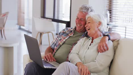 senior caucasian couple having a video call on laptop while sitting on couch at home