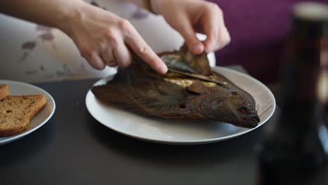 person peel skin of freshly cooked delicious fish, close up handheld view