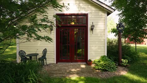 push-in-shot-of-the-exterior-of-a-white-school-house-with-red-doors-on-a-sunny-day-with-trees-in-the-foreground