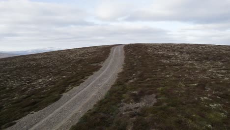 cinematic aerial drone footage flying fast and low over wild heather, grouse moorland and a 4x4 track to reveal a mountain landscape with patches of snow