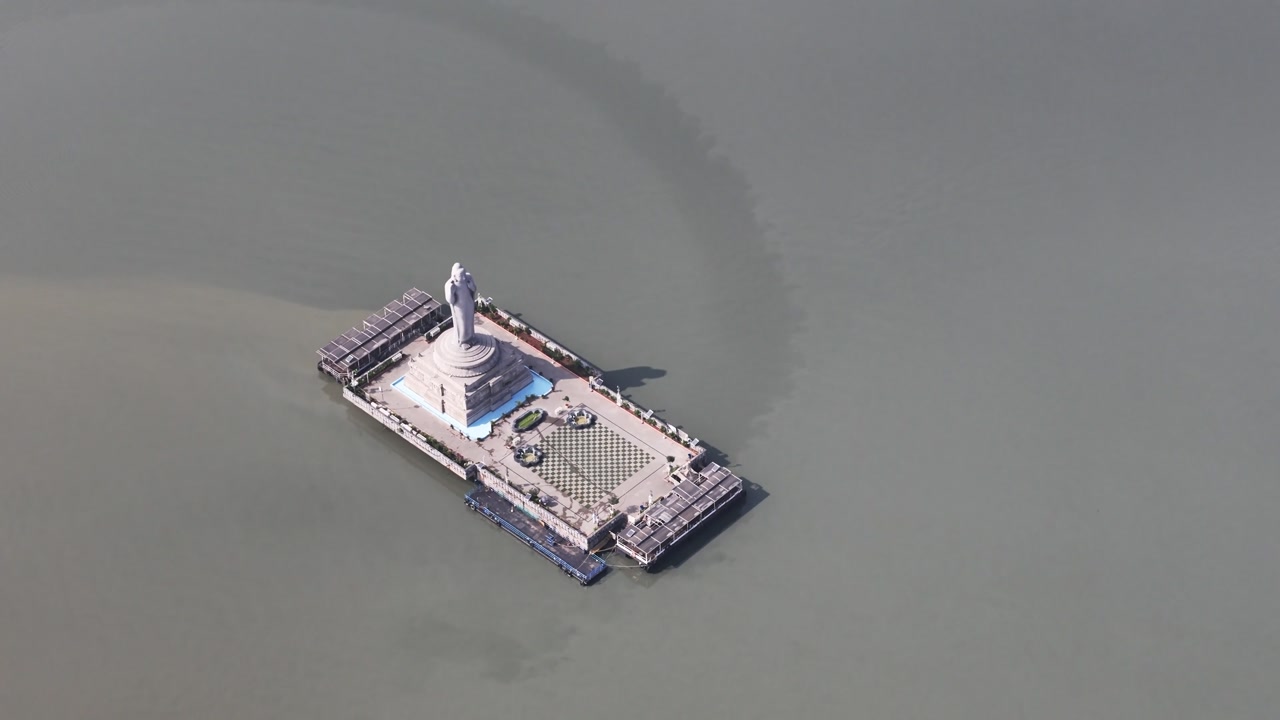 Drone shot capturing the Buddha statue platform in Hussain Sagar with symmetrical design, calm waters, and minimal surroundings.