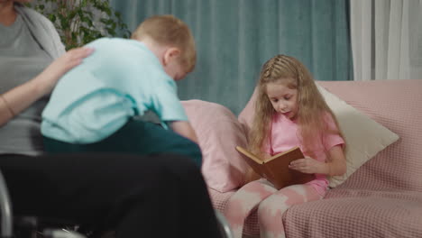 boy sits on lap of mother in wheelchair while girl reading