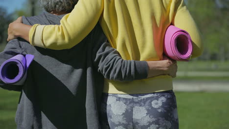 vista trasera de mujeres abrazándose unas a otras con una alfombra de yoga en las manos