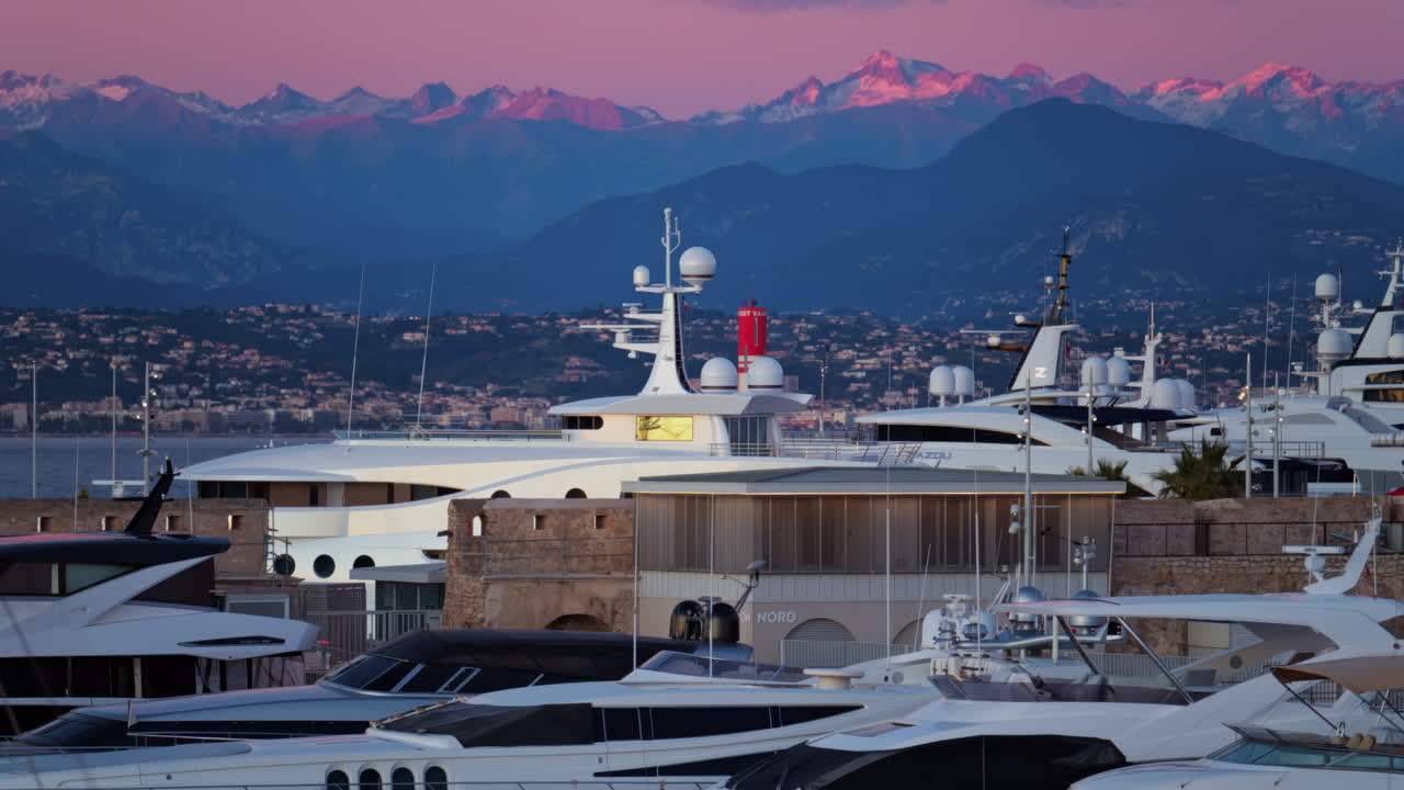 Multiple white boats docked in the Port Vauban, Antibes, France with the mountains on the background at sunset