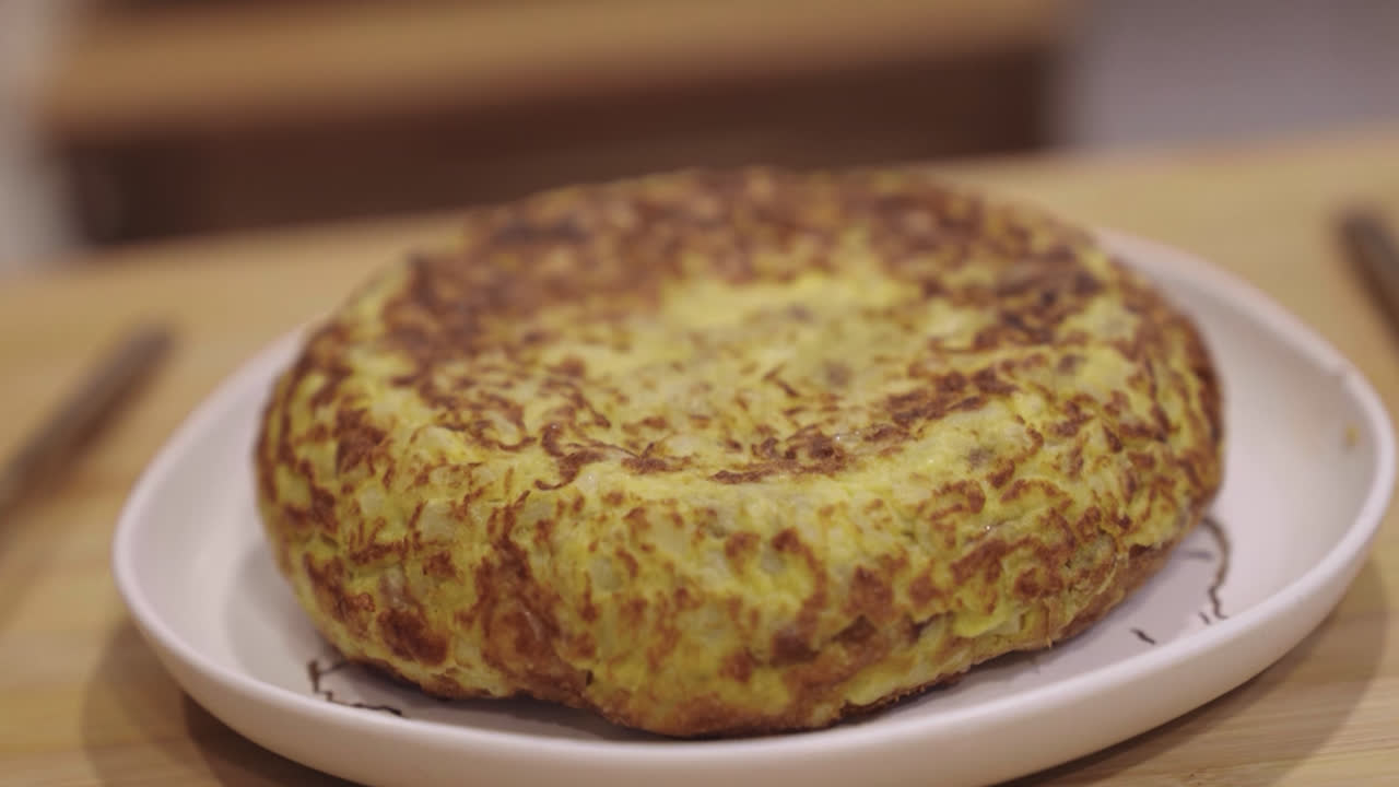 Beautiful slow motion close-up shot of a beautiful typical Spanish potato omelette on a kitchen table inside a brightly lit house.