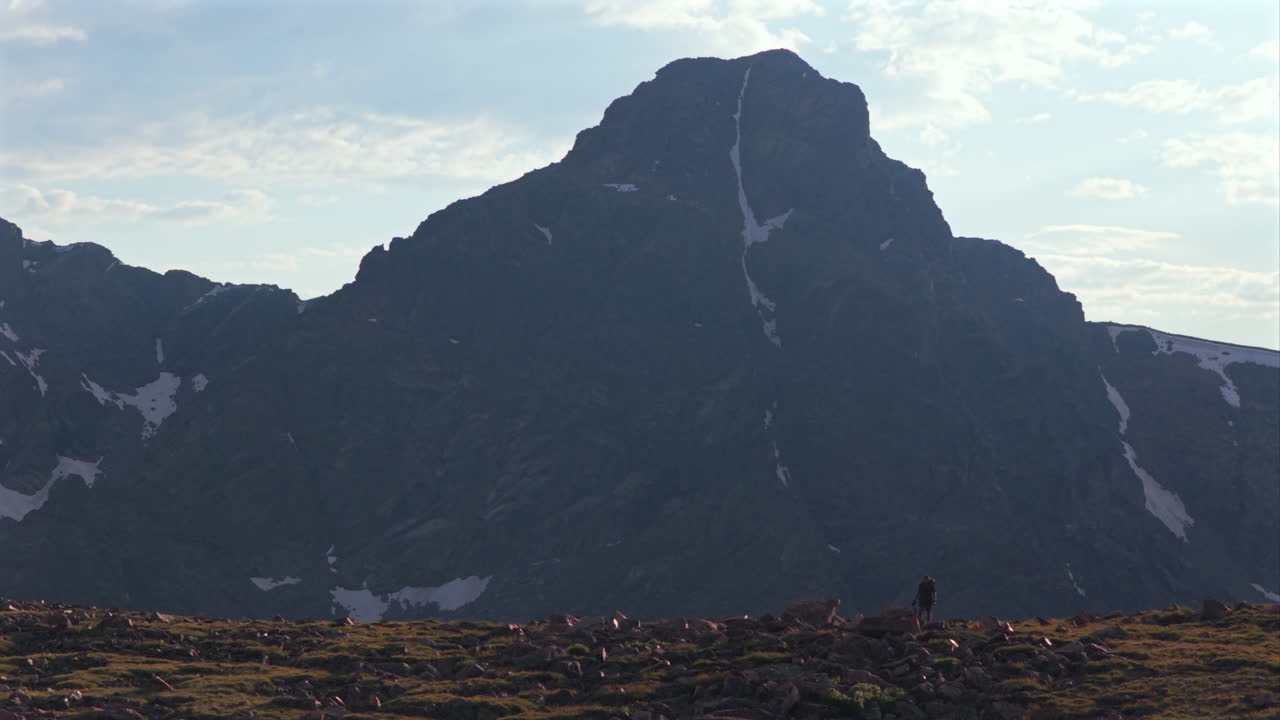 Hiker walking Notch Mountain shelter Halo Ridge landscape view of Mount of the Holy Cross 14er peak wilderness aerial drone Colorado summer afternoon sunset clouds Rocky Mountains Sawatch Range