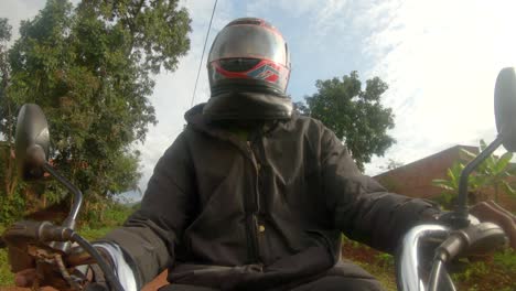 A-action-shot-of-an-African-man-wearing-a-helmet-while-steering-a-motor-bikes-handle-bars-rides-through-a-African-village