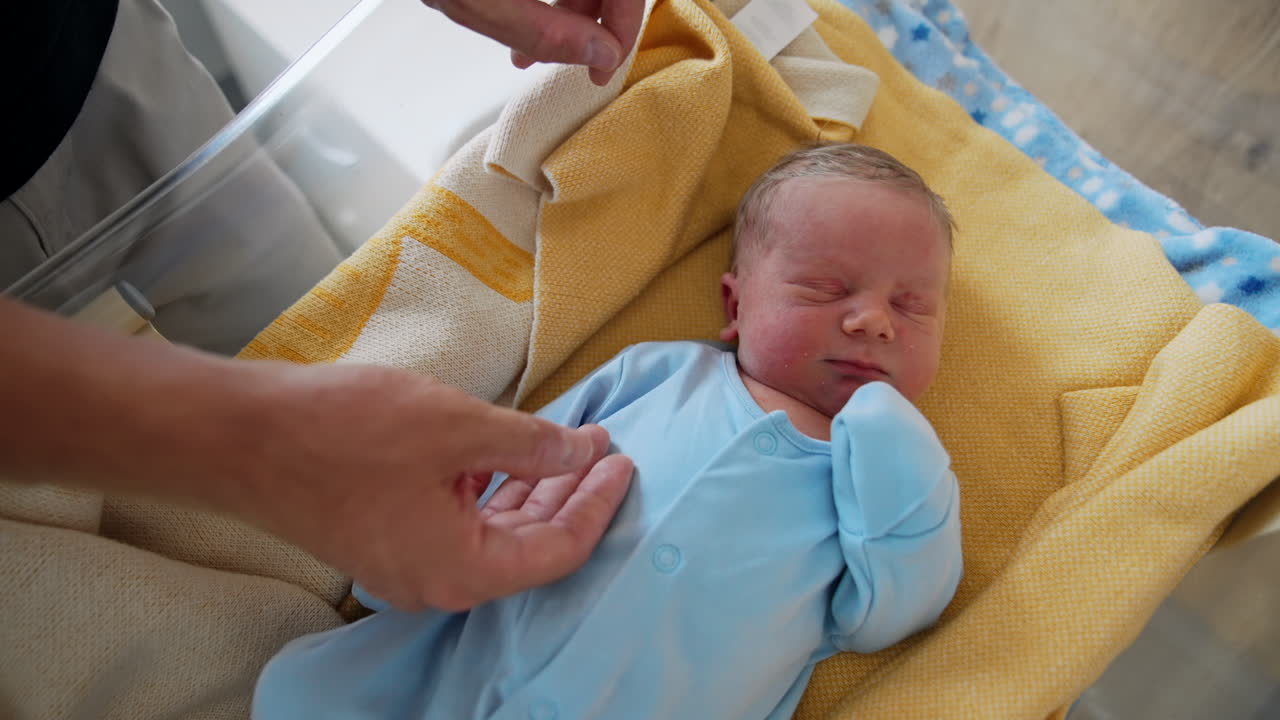 Adorable newborn child sleeping sweetly. Father's hand stroking a baby in a blue romper. Top view.