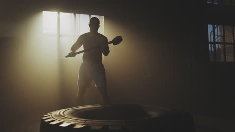 man hammering tire in gym