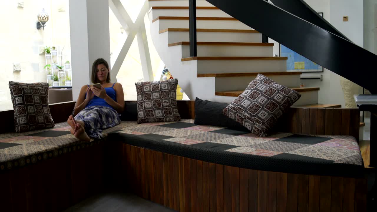 una mujer en casa está acostada en el sofá con un teléfono inteligente