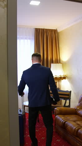 man comes into the hotel room. businessman with a suitcase entering the room. journey for business. back view. vertical video