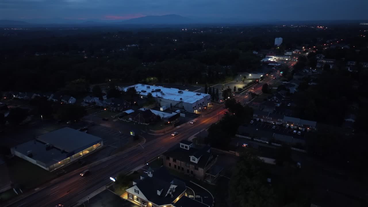 Vista aerea di una strada suburbana americana al crepuscolo con lampioni luminosi, auto sulla strada ed edifici commerciali. Scena di traffico nell'atmosfera di una piccola città degli Stati Uniti. Paesaggio notturno in Virginia