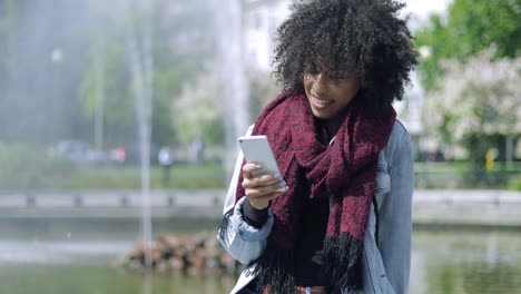 Lächelndes-Mädchen-Mit-Telefon-Am-Brunnen