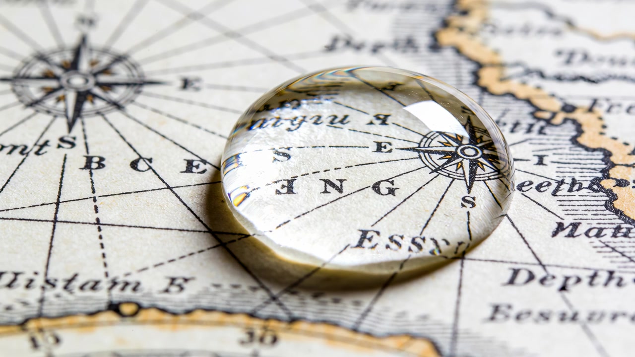 Resting clear sphere magnifying compass rose on antique nautical chart, reflecting overhead light