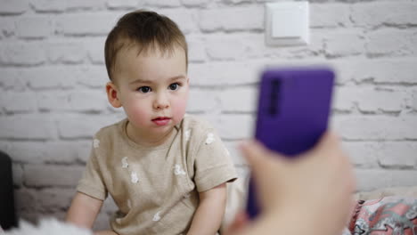 unknown holding a phone in front of a cute toddler. little kid is absolutely absorbed by the gadget.