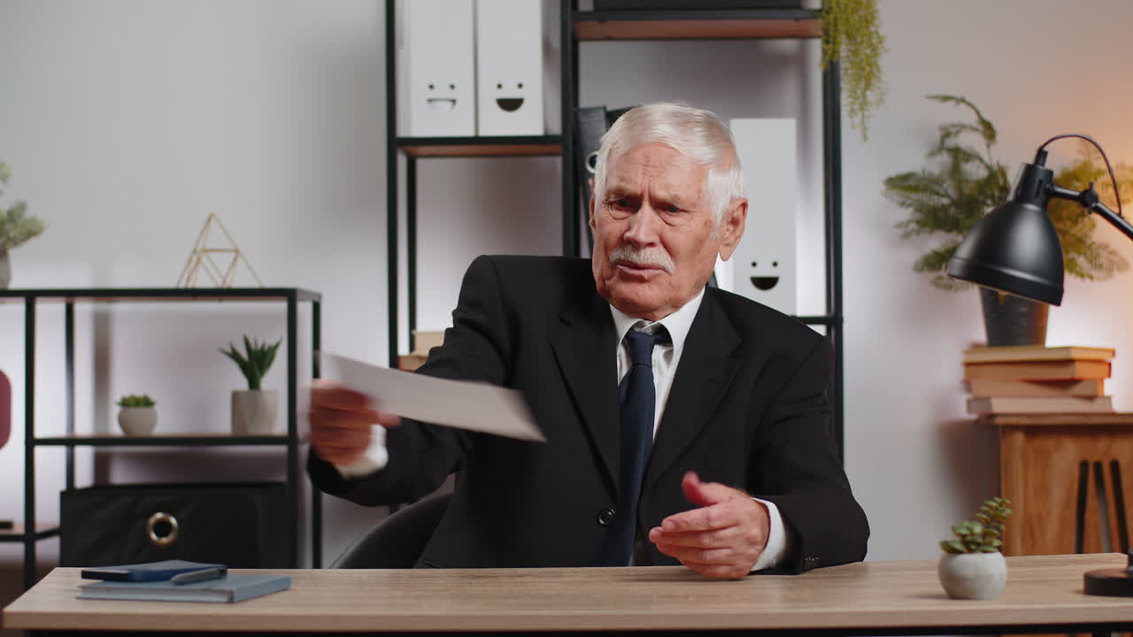 Shocked senior businessman opening envelope reading bad news in letter feels upset at office table