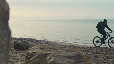 Man-rides-his-mountain-bike-along-calm-sandy-beach-during-morning-hours