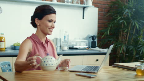 una mujer vertiendo té en una taza durante una llamada de video. una chica usando una computadora portátil para hablar por video.