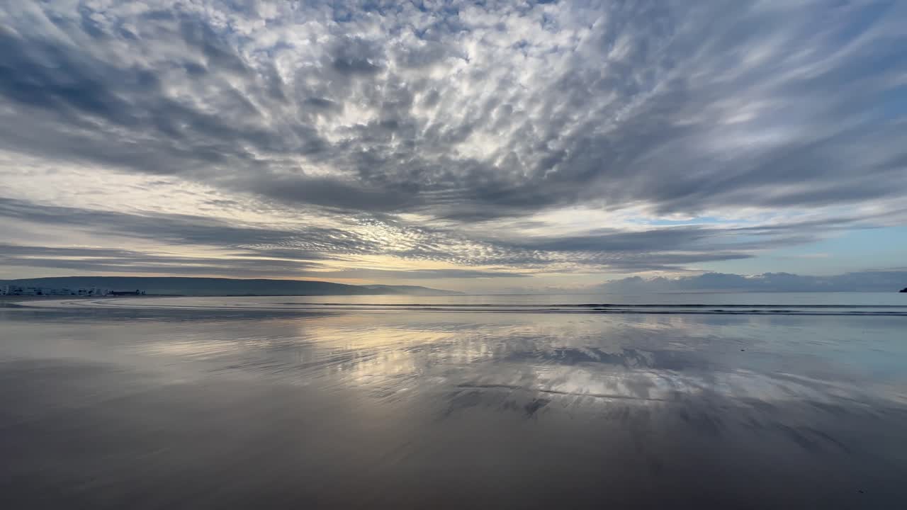 Golden sunrise reflecting on the wet sand of Barbate beach, with dramatic clouds and a distant ship sailing on the horizon, creating a serene and peaceful atmosphere