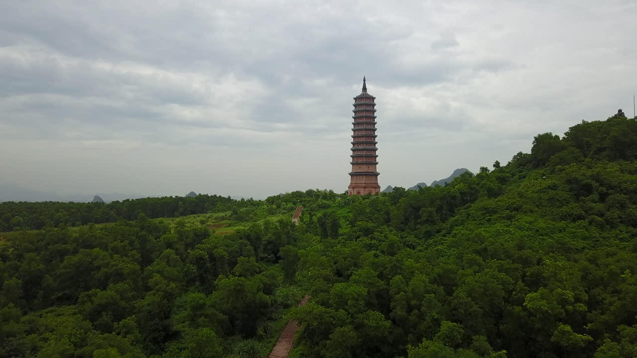 Experience a sweeping panoramic view of the forest path leading to the majestic Bái Đính Pagoda in Ninh Binh, Vietnam, under a soft, overcast sky. Discover the natural beauty surrounding.