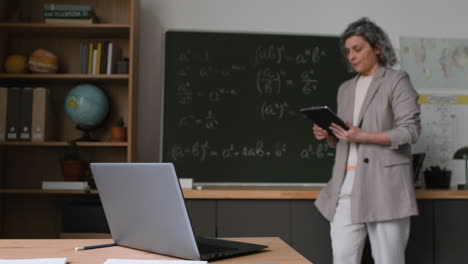 teacher in a classroom with tablet and laptop