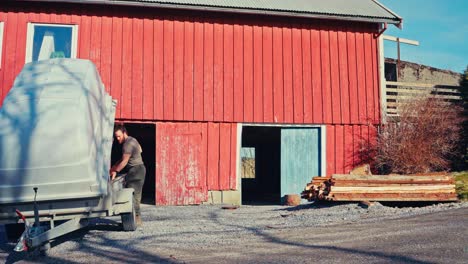 a person unloads timber beside a red barn, preparing materials for a day of work - static shot