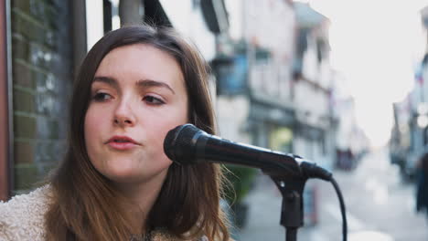 female musician busking playing acoustic guitar and singing outdoors in street