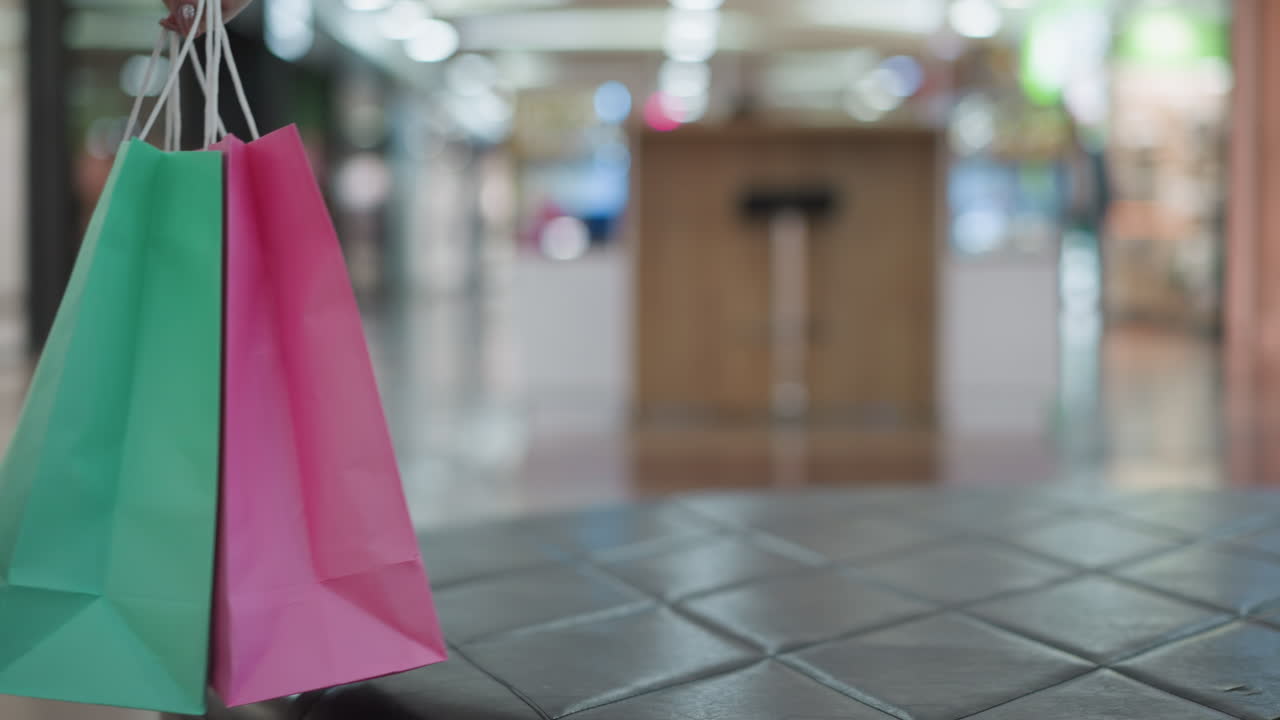 가죽 좌석에 있는 활기찬 쇼핑 가방의 클로즈업, 잘 조명된 쇼핑몰에서 그들을 잡기 위해 손을 는, 소비자 활동과 소매 환경을 보여주는