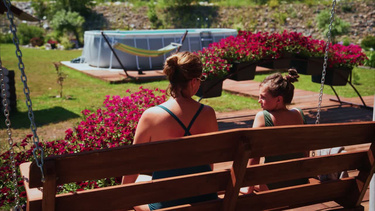 Two Women Relaxing on a Garden Swing on a Sunny Day