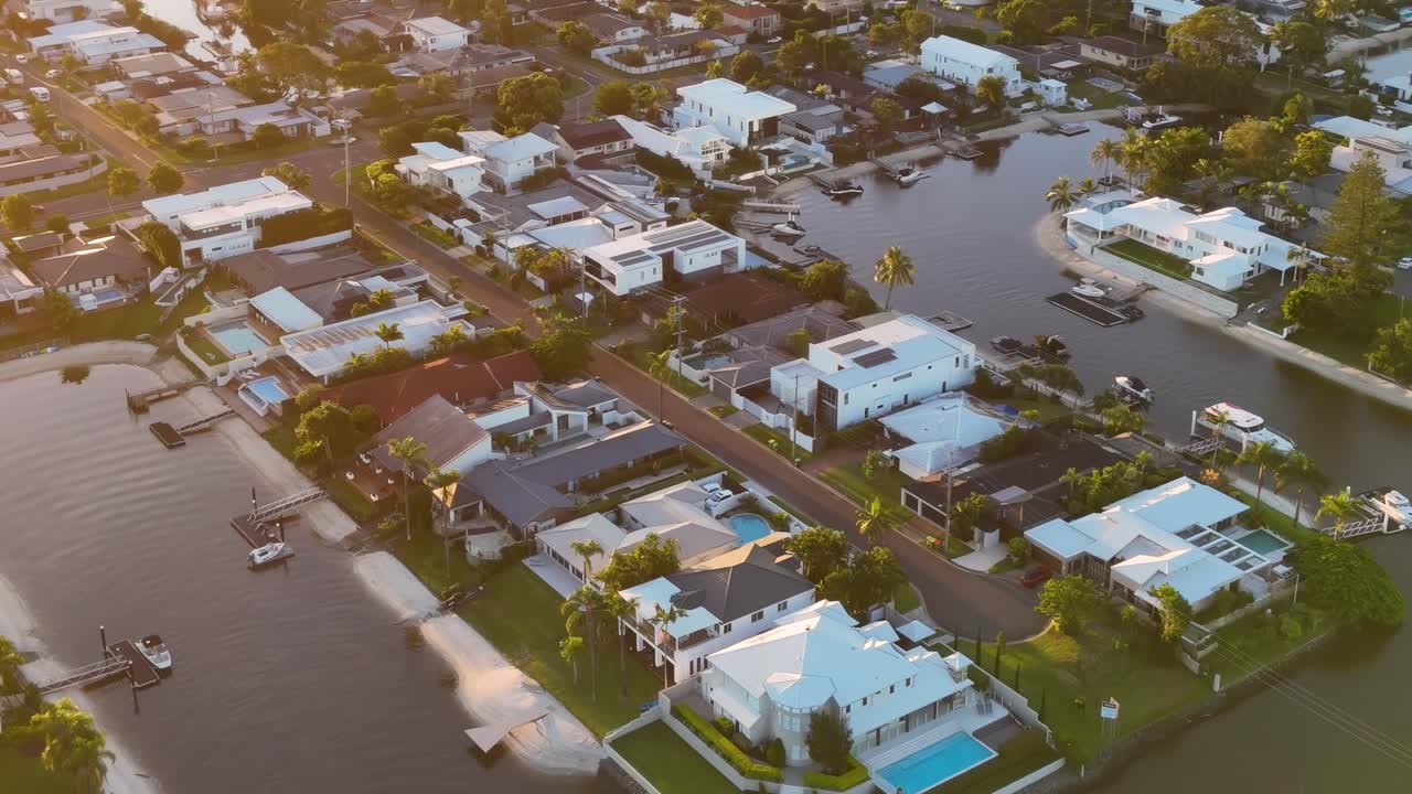 Drone footage showcasing waterfront residential area with canals and modern homes during sunset.