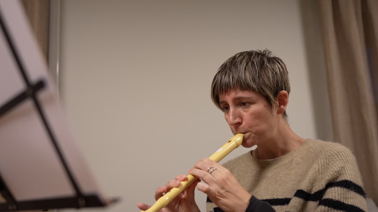 Woman Playing Recorder and Reading Sheet Music Indoors