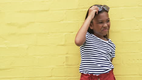 a young african american girl stands against a yellow background with copy space