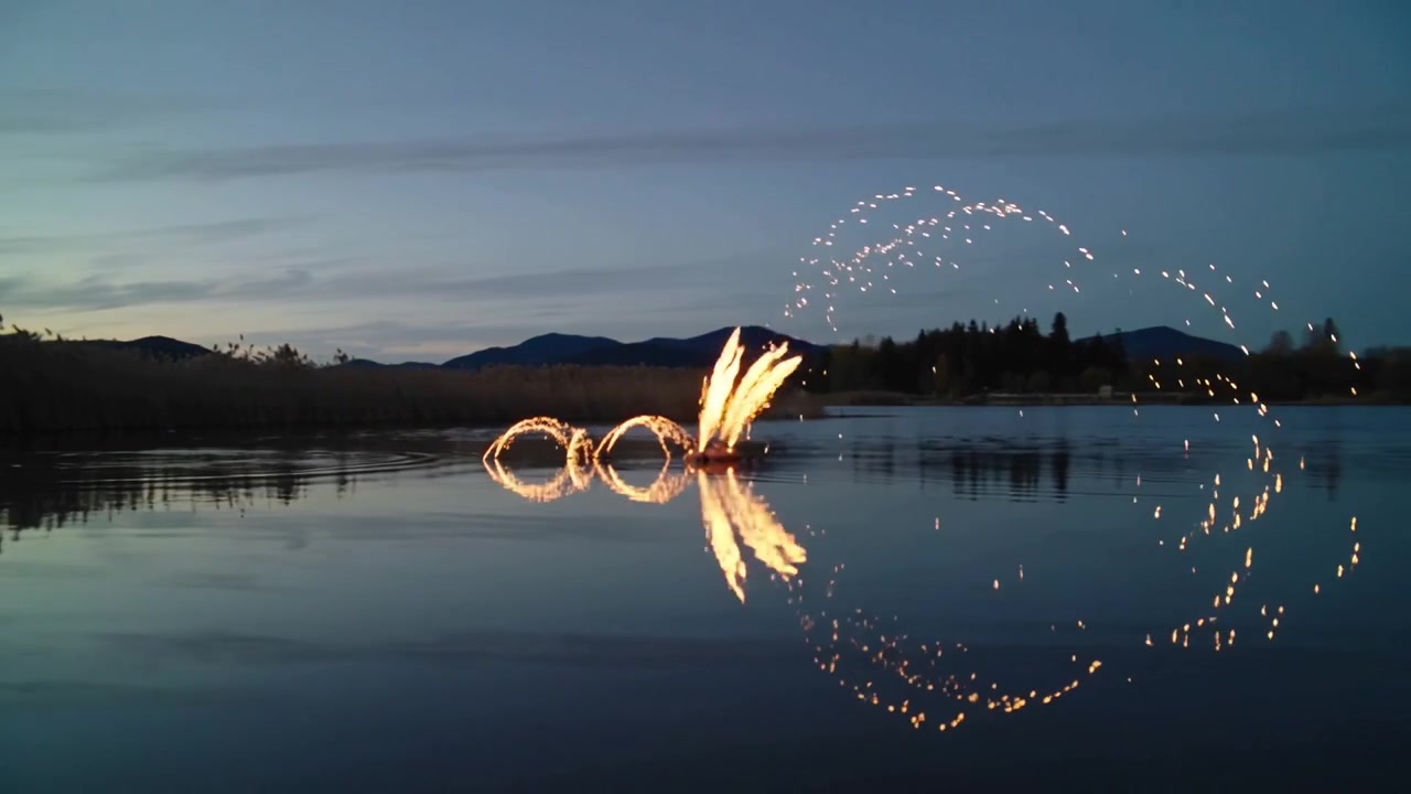 Una fonte che si accende creando tre cerchi e scintille ad arco sulla riva al tramonto, formando riflessi calmi sul lago