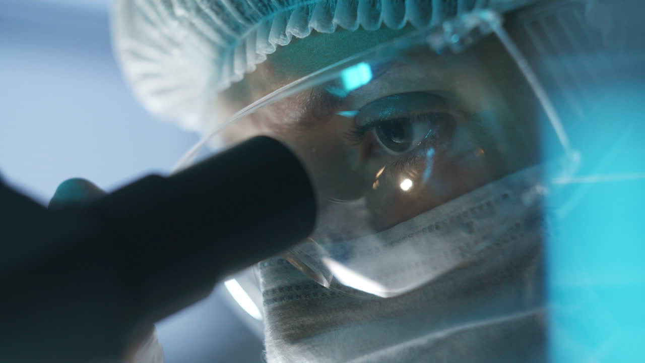 Lab Scientist in Mask and Goggles Examining Sample through Microscope