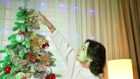 decorating a christmas tree at home. a woman joyfully arranges ornaments on a christmas tree at home during the holiday season