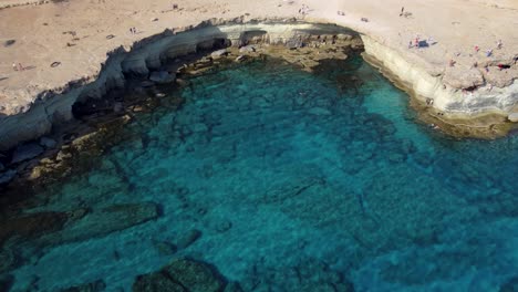 Inclinación-Aérea-Acercándose-A-Aguas-Cristalinas-En-La-Bahía-De-Cuevas-Marinas,-Chipre