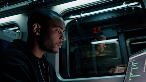 a young man is focused intently on his laptop as he rides the late-night train through the bustling urban cityscape
