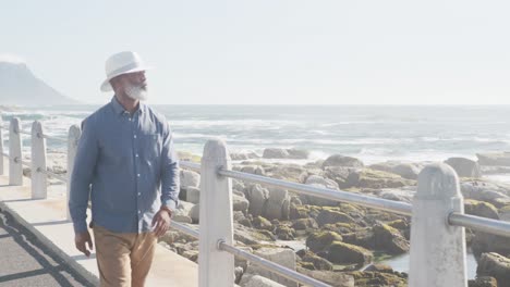 happy senior african american man walking along promenade by the sea, slow motion