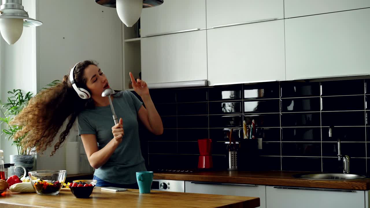 Giovane donna allegra e divertente che balla e canta con un mestolo mentre si gode il tempo libero in cucina a casa.
