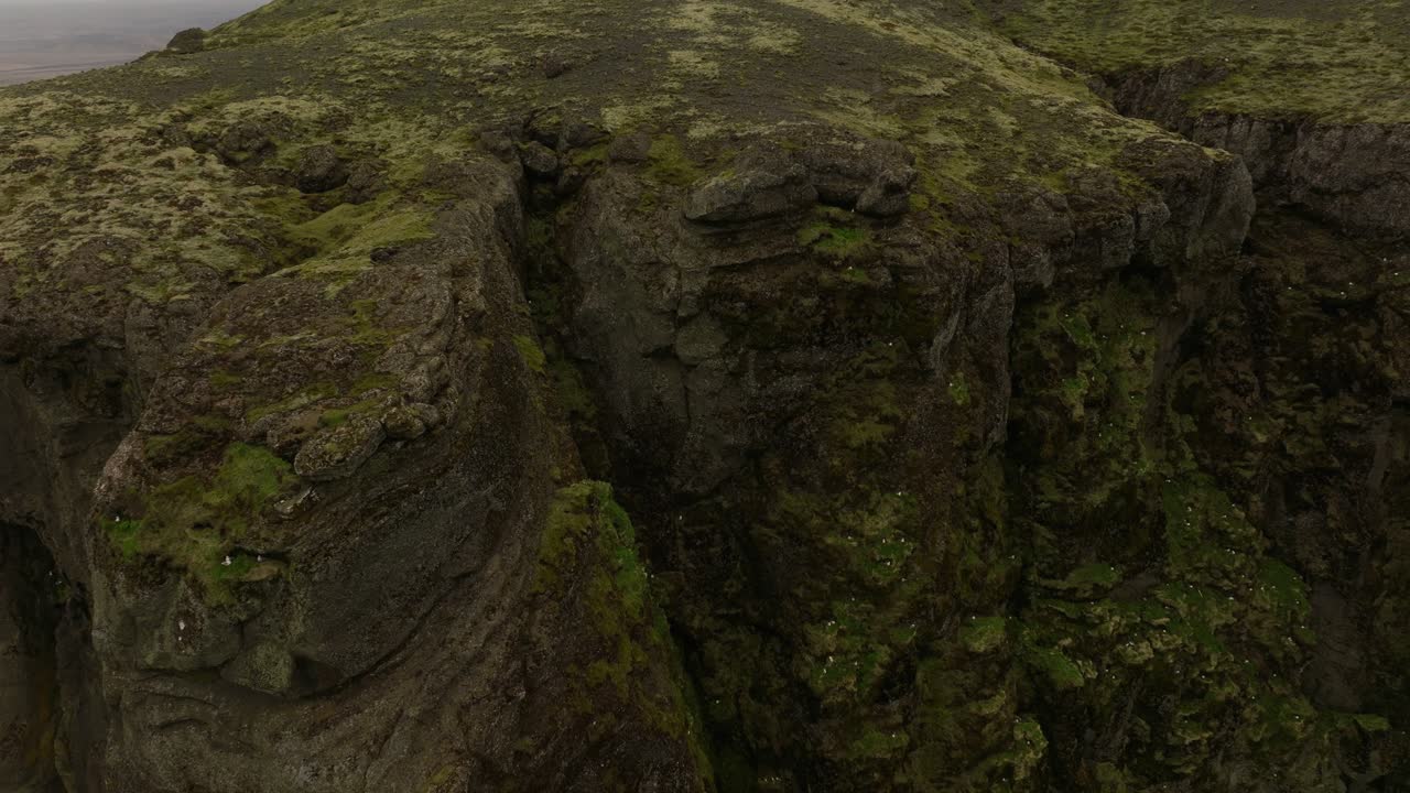 Close-up aerial view of the rugged cliffs at Petursey, Iceland, showcasing the moss-covered rock formations and deep crevices in the volcanic landscape.