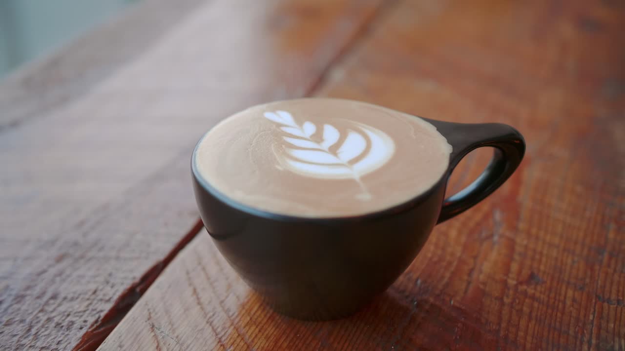 Handheld static shot of cute latte art in black cup on wooden table