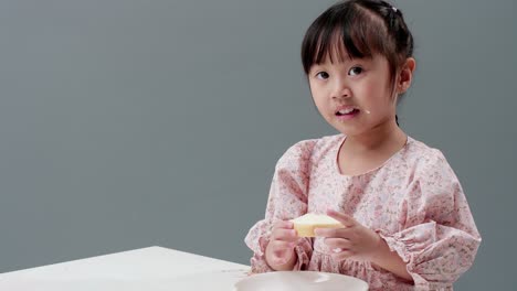 asiatic child eating piece of sweet in the studio with a gray background